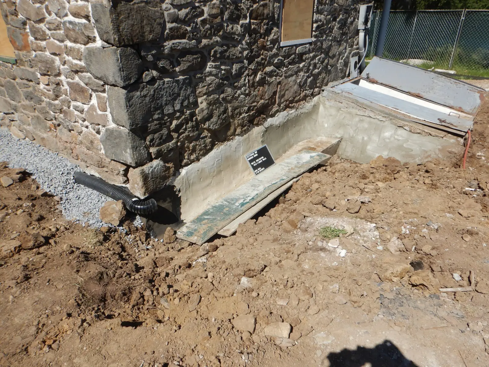 Excavated stone house foundation with waterproofing, gravel, and a black drain pipe at the footing