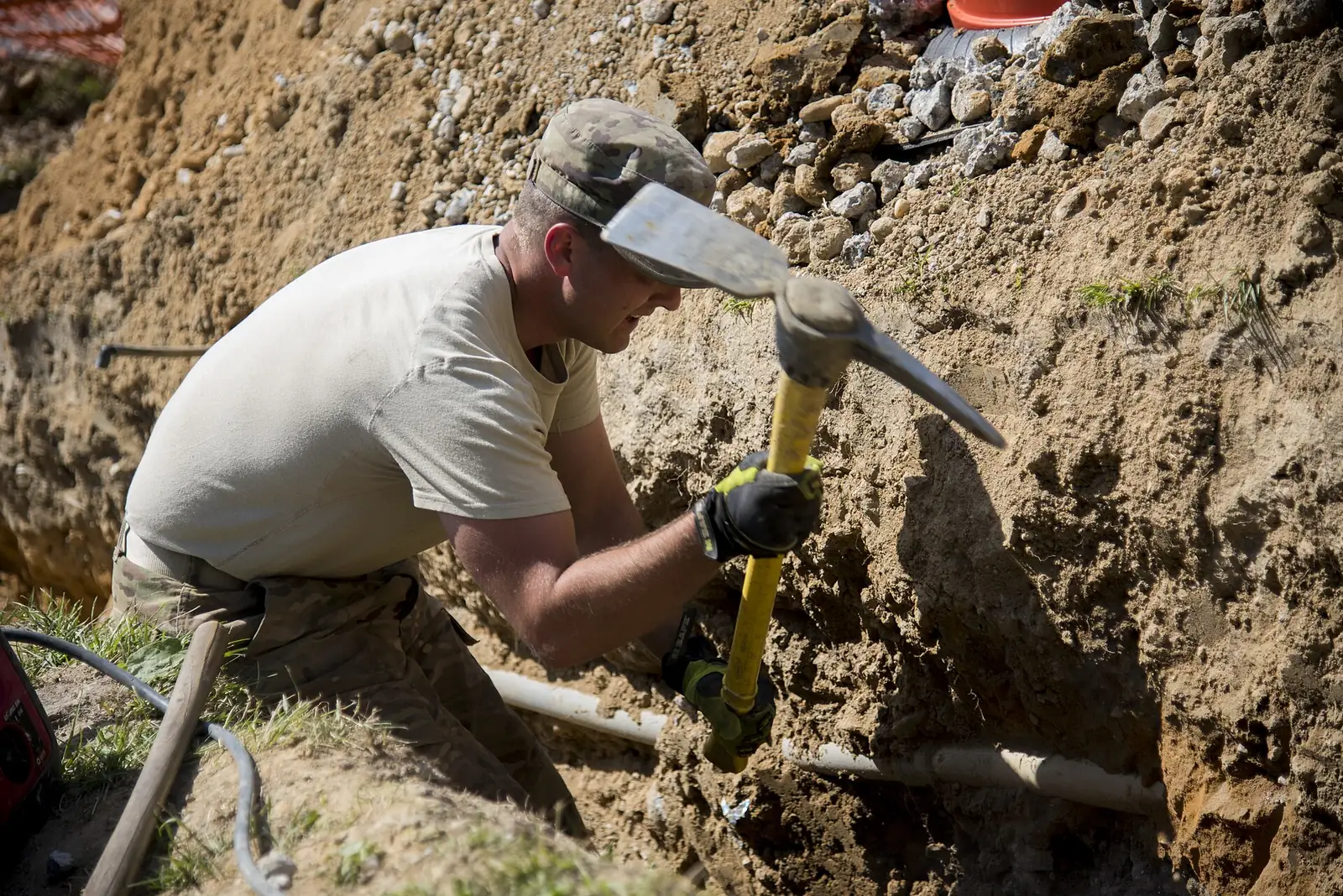 Worker using a pickaxe to dig out a trench for a French drain installation