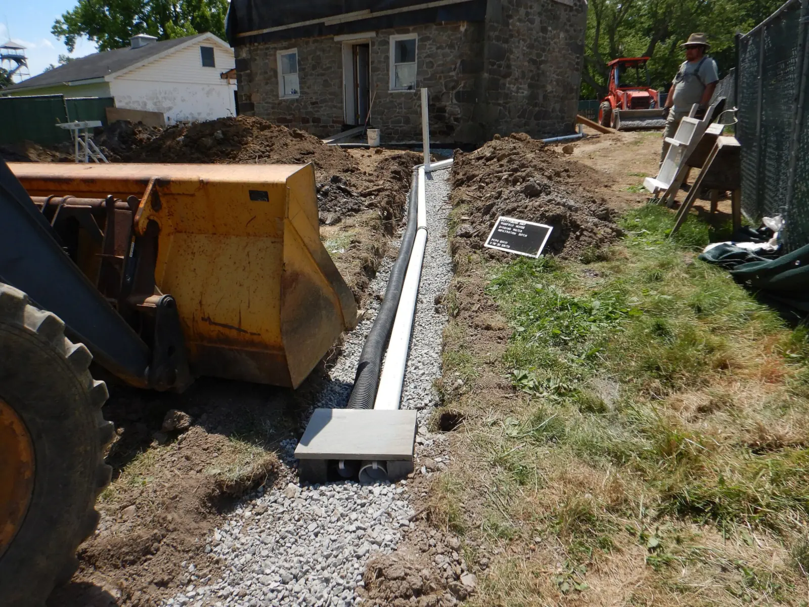 Gravel-lined drainage trench with corrugated drain pipe and PVC pipe running across a yard