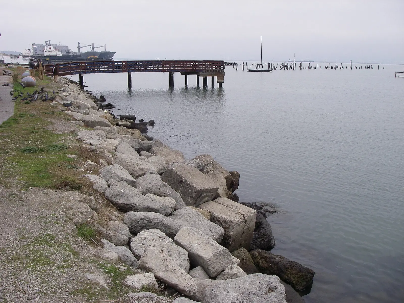 Large riprap rocks armoring a bay shoreline beside a walking path and fishing pier