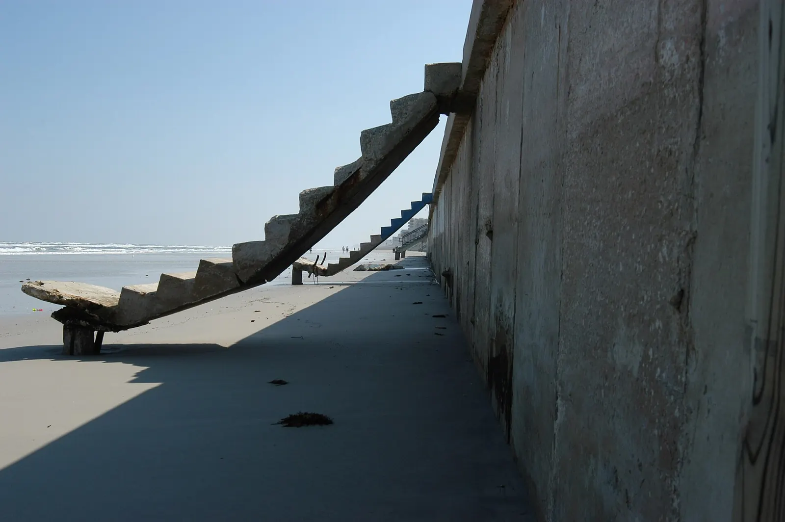 Exposed concrete seawall face with panel joints and staining after storm scour removed the sand